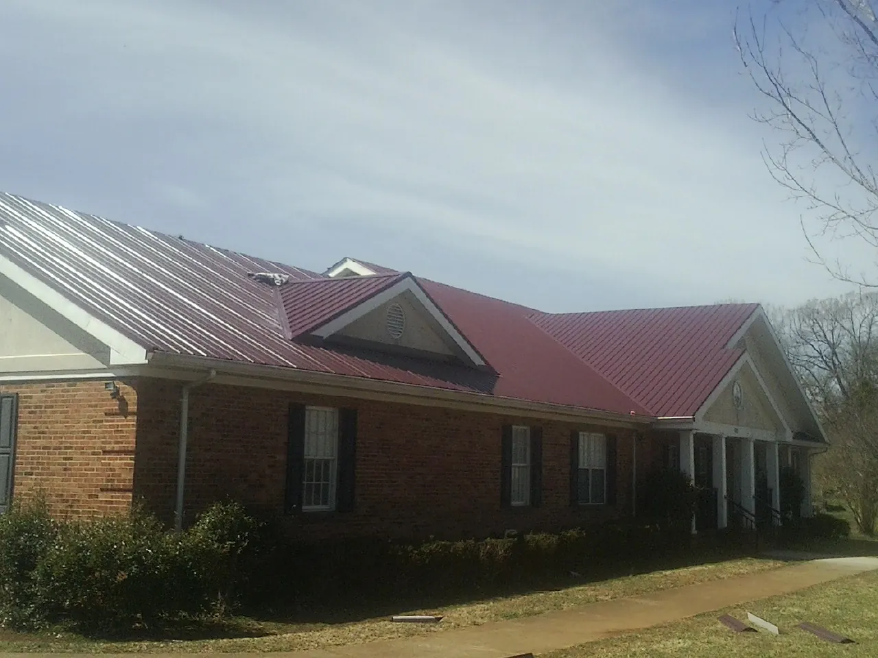 Red metal roof with gabled entries on a long brick building, from a Hail Damage Roof Repair job in Culpeper