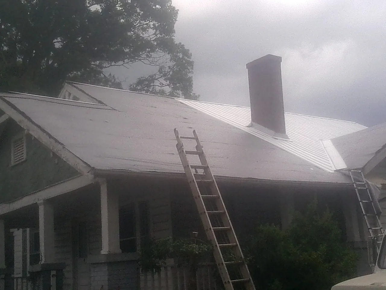 Ladders against a metal roof on an older home with a brick chimney in Culpeper