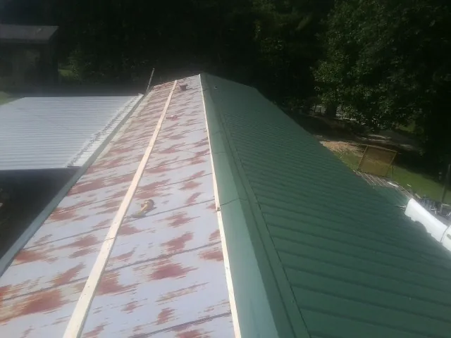 Old rusted panels beside newly installed green metal roofing — Wind Damage Roof Repair by Roofing Brothers in Culpeper