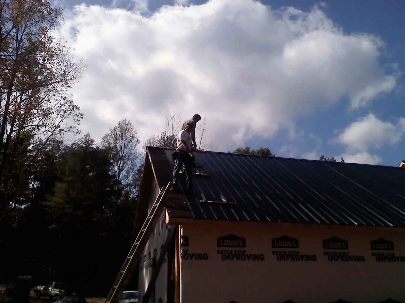 Roofer fastening dark metal panels high against a cloudy sky, from a Roof Inspection job in Culpeper