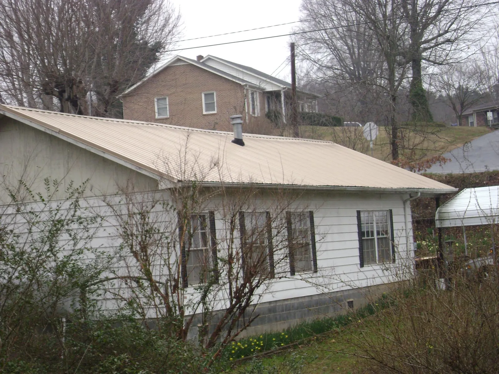 Tan metal roof on a white sided house set into a hillside — Commercial Roofing by Roofing Brothers in Culpeper